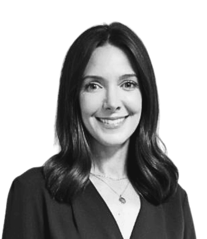 Black and white photo of a woman with shoulder-length dark hair, wearing a V-neck top and a necklace, smiling at the camera against a plain background.